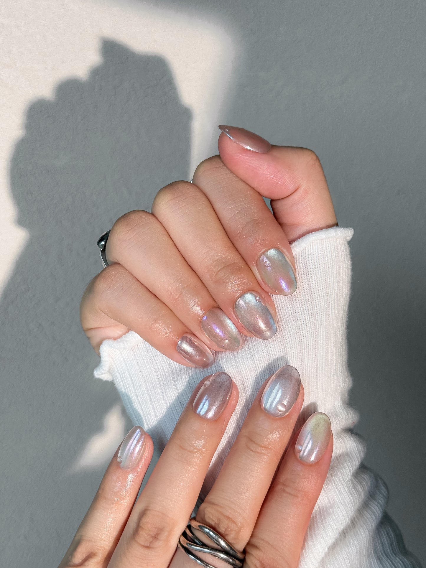 Détail des ongles Perle de Tahiti avec effet goutte d’eau et éclat nacré multicolore.