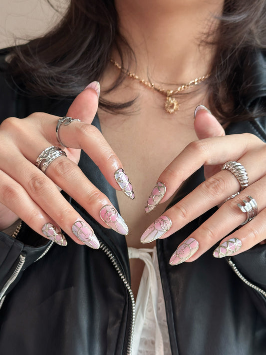 Press-on nails Vitra portés, avec dégradé rose, lignes métalliques effet vitrail et forme amande longue.