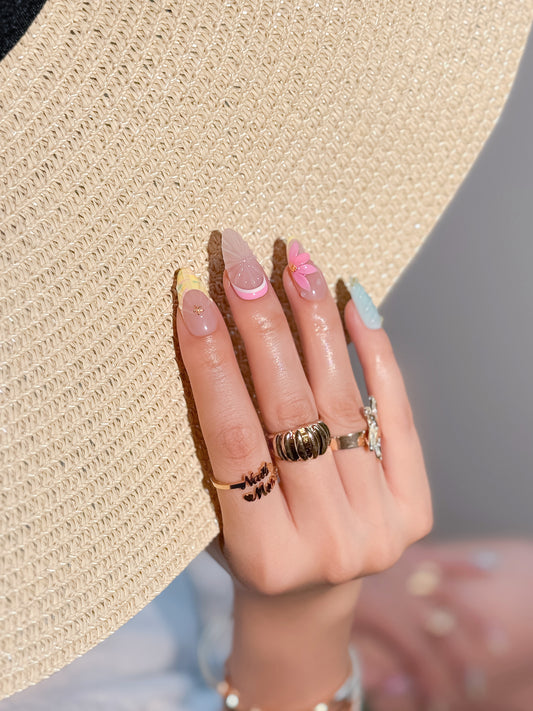 Coquélia, ongles press-on pastel portés sur les mains, avec détails coquillage, fleur et finition brillante.