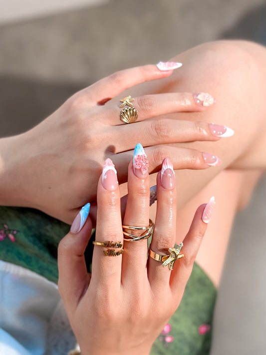 Manucure Côte Fleurie portée, faux ongles floraux rose pastel et bleu avec détails perlés par NailMusee