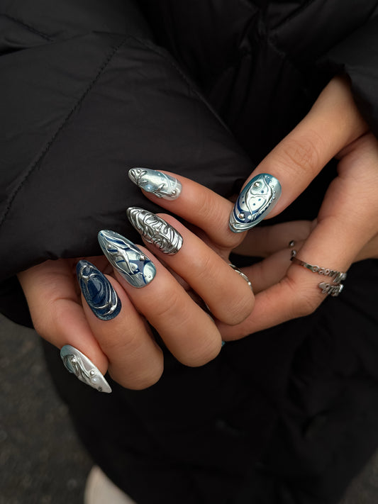 faux ongles bleu et argent portés sur main avec effet chrome brillant
