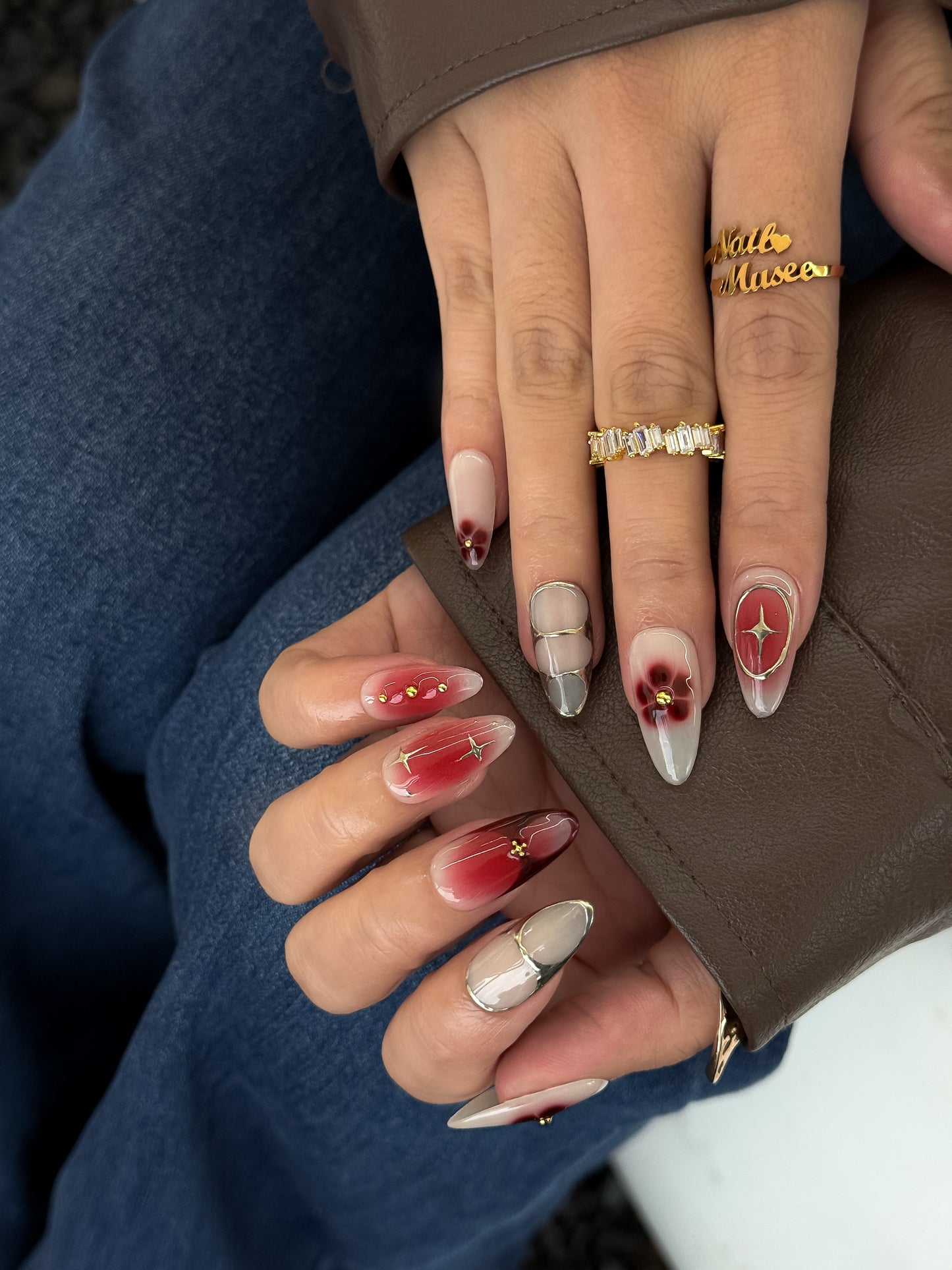 Close-up of hands wearing Rouge Bohème press-on nails by NailMusee，featuring red ombré, nude tones and floral accents.