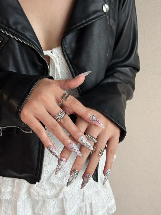 Press-on nails Relique Rose portés, avec dégradé rose, détails chrome en relief et forme stiletto longue.